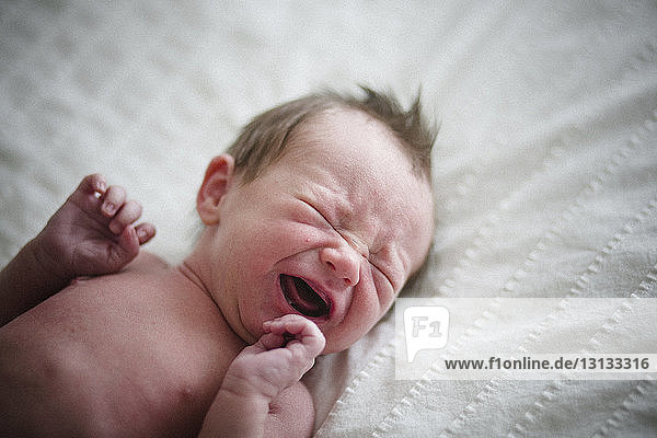 Hochwinkelaufnahme eines hemdlosen Neugeborenen  der zu Hause im Bett weint