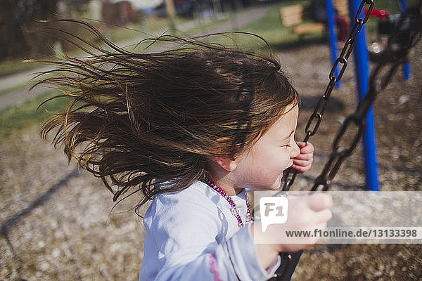 Side view of playful girl swinging at playground