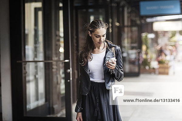 Front view of woman using phone while standing on sidewalk