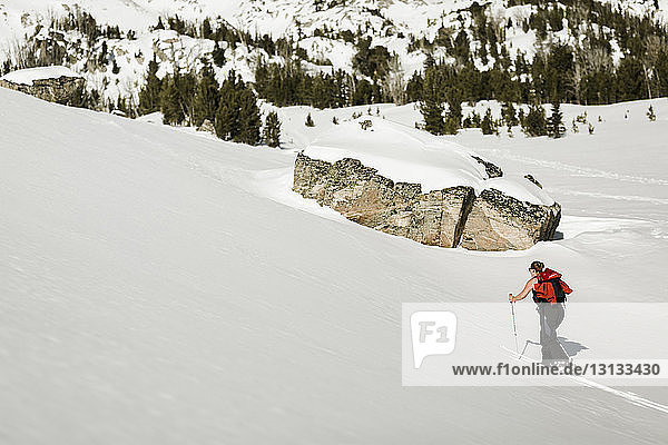 Wanderin mit Rucksack besteigt schneebedeckten Berg mit Wanderstöcken