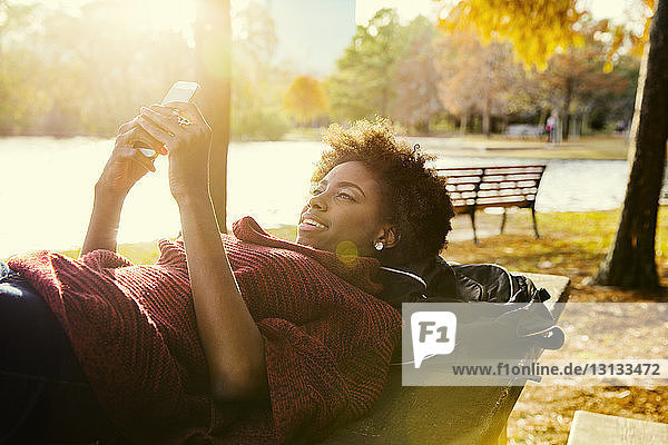 Junge Frau telefoniert  während sie auf einer Parkbank liegt