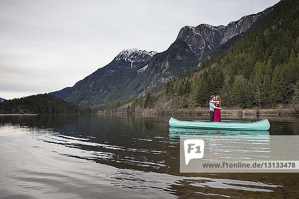 Young couple embracing while standing in canoe on lake against mountains