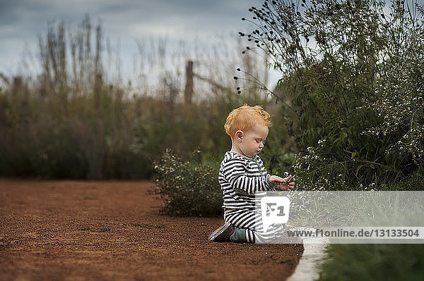 Seitenansicht eines kleinen Jungen  der einen Stock hält  während er im Park kniet
