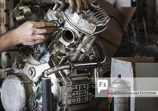 Beschnittenes Bild von Händen beim Reinigen des Motorradmotors in der Werkstatt