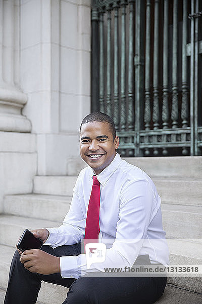 Portrait of smiling businessman holding mobile phone while sitting on steps