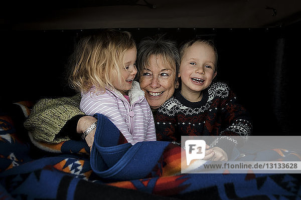Lächelnde Großmutter mit Enkelkindern sitzt im Dachzelt auf dem Auto