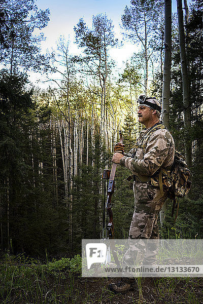 Side view of hunter holding bow and arrow while standing in forest