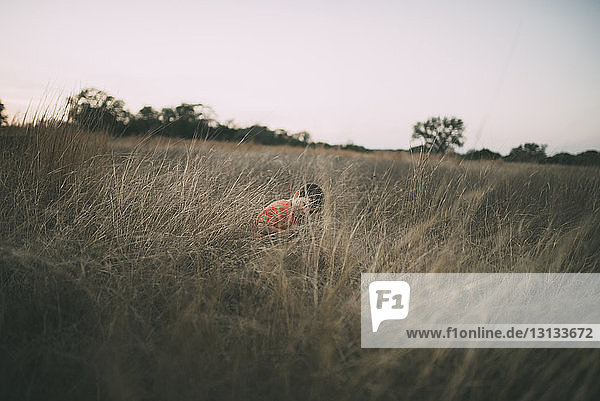 Boy sitting amidst dried grass field