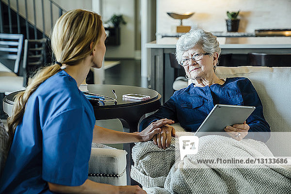 Senior woman looking at home caregiver while holding tablet computer in living room