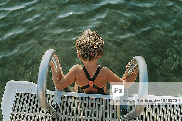 Hochwinkelaufnahme eines Mädchens in Badebekleidung  das auf einer Leiter im See sitzt