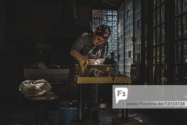 Female craftsperson making clay pot in darkroom