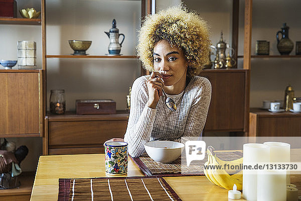 Porträt einer selbstbewussten Frau  die den Löffel hält  während sie im Haus am Tisch sitzt
