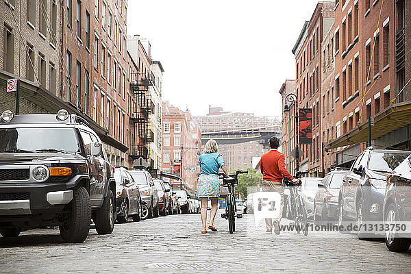 Rückansicht eines erwachsenen Paares zu Fuß mit Fahrrädern auf der Straße in der Stadt