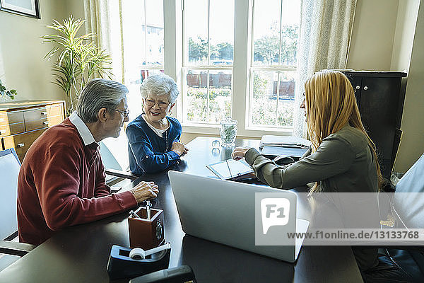 Financial advisor explaining plan to senior couple on tablet computer while sitting in office