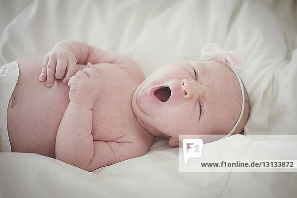 Baby wearing headband yawning while lying on bed at home