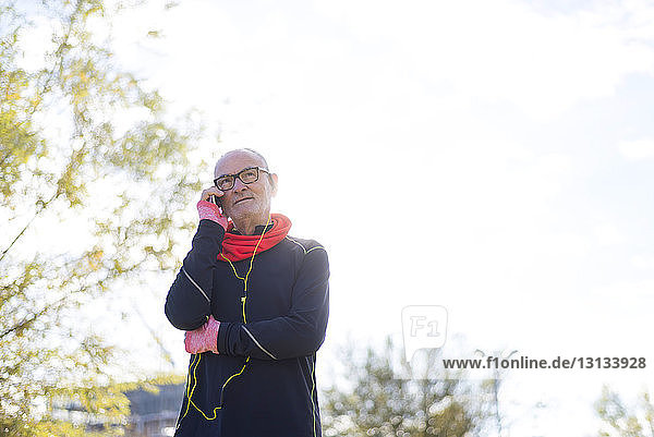 Älterer Mann trägt Sportkleidung  während er ein Smartphone gegen den Himmel im Park abhebt