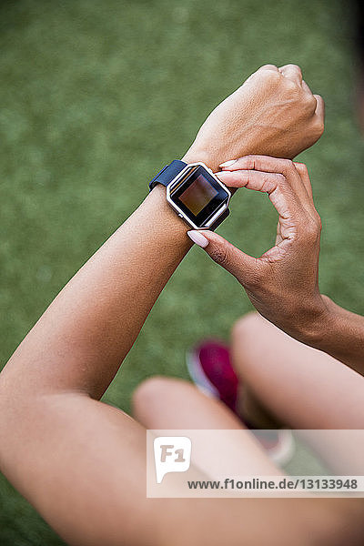 Hochwinkelaufnahme einer Sportlerin mit einer intelligenten Uhr  die auf einem Rasenplatz sitzt