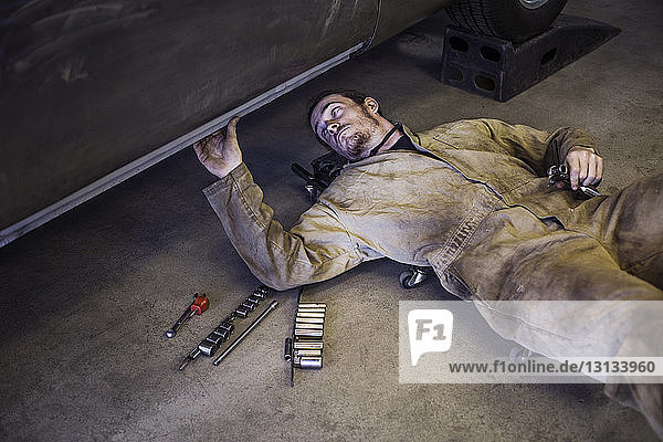 Hochwinkelansicht eines Mechanikers  der in einer Autowerkstatt auf einem Kriechwagen liegt