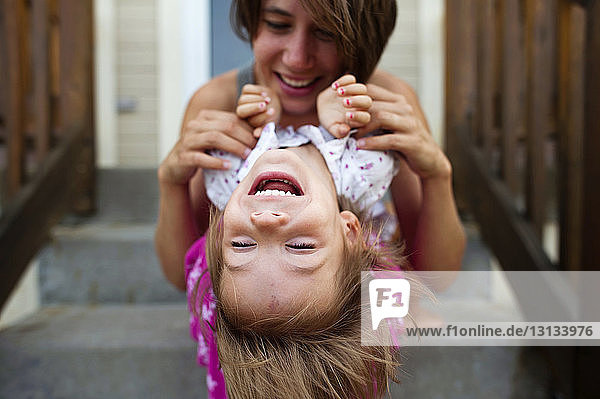 Fröhliche Mutter spielt mit der Tochter  während sie auf Stufen sitzt