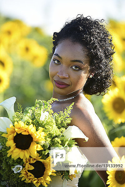 Portrait einer Braut  die einen Blumenstrauss hält  während sie auf dem Bauernhof vor Sonnenblumen steht