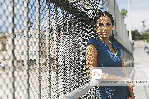 Portrait of sportswoman leaning on chainlink fence
