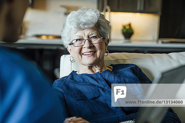 Glückliche ältere Frau schaut im Wohnzimmer auf die häusliche Pflegekraft