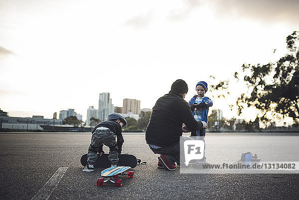 Vater hilft Söhnen bei der Vorbereitung auf das Skateboarden auf dem Feld