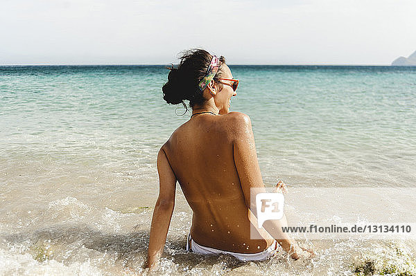 Rear view of shirtless woman sunbathing at beach