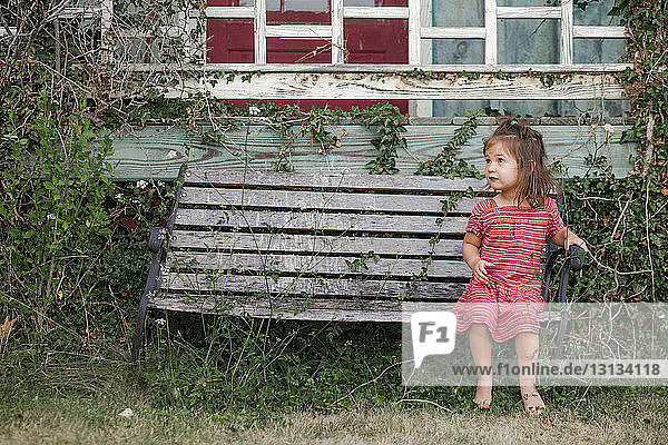 Ein süßes Mädchen in voller Länge sitzt auf einer verlassenen Parkbank