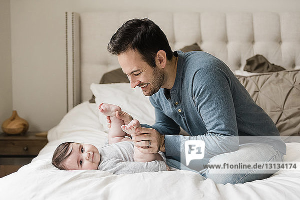 Father playing with son while sitting on bed at home