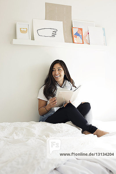 Happy woman holding diary while sitting on bed at home