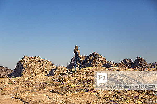 Rear view of woman walking on rocks against clear blue sky