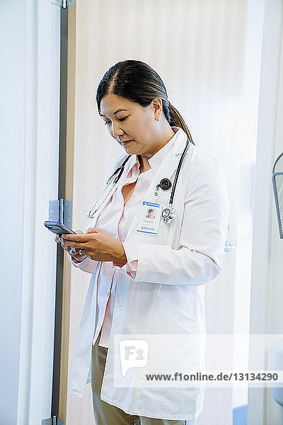 Ärztin benutzt Smartphone  während sie im Krankenhaus gegen die Tür steht