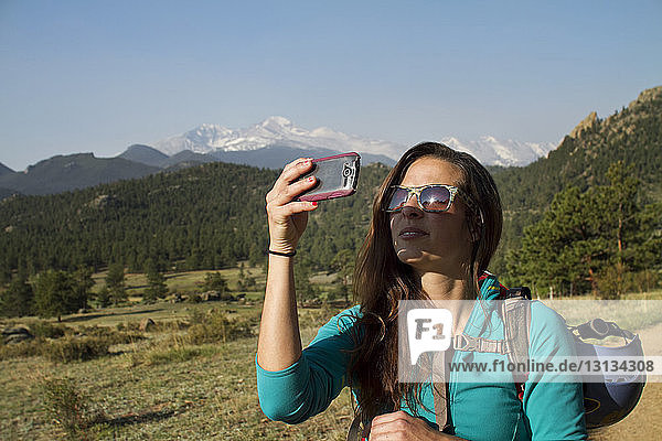 Woman photographing with smart phone while standing against mountain