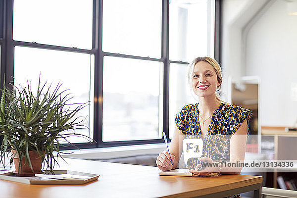 Portrait of smiling businesswoman with mobile phone sitting at table in office