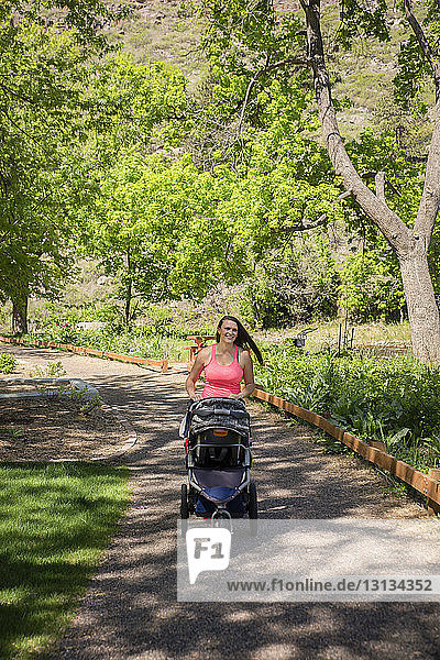 Frau mit Kinderwagen geht im Sommer auf einem Fußweg im Park spazieren
