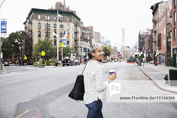 Portrait of woman holding coffee cup while walking on street