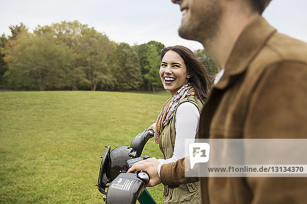 Cheerful couple talking while walking with bicycles in park