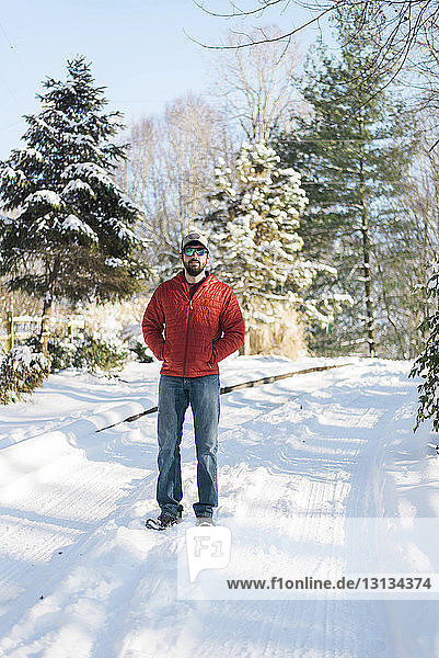 Portrait of man wearing sunglasses while standing on snow covered field in forest
