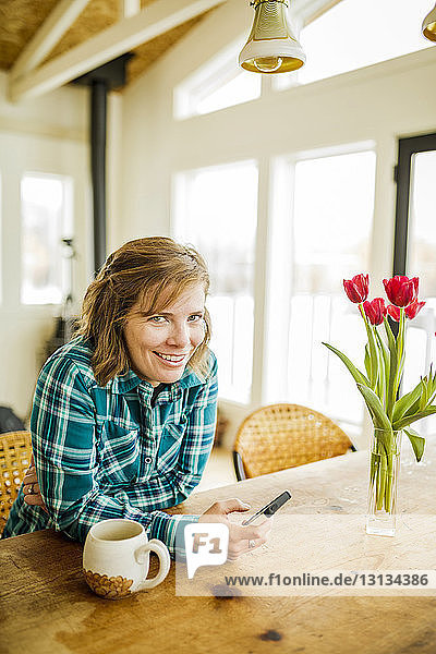 Porträt einer Frau  die ein Smartphone benutzt  während sie zu Hause am Tisch sitzt