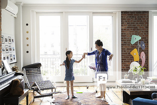 Mädchen und Mutter halten sich an den Händen und tanzen zu Hause auf dem Teppich