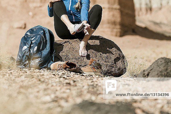 Niedriger Teil des Wanderers beim Ausziehen der Socken  während er auf einem Felsen in der Wüste sitzt