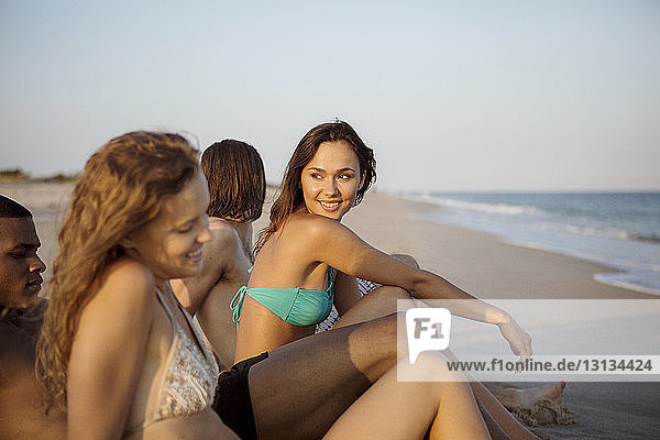 Lächelnde Frau sitzt mit Freunden am Strand