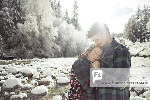 Portrait of woman embracing man while standing in forest at Lynn Canyon Park during winter
