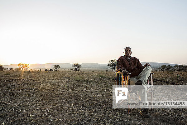 Portrait of smiling man sitting on chair at Serengeti National Park against clear sky