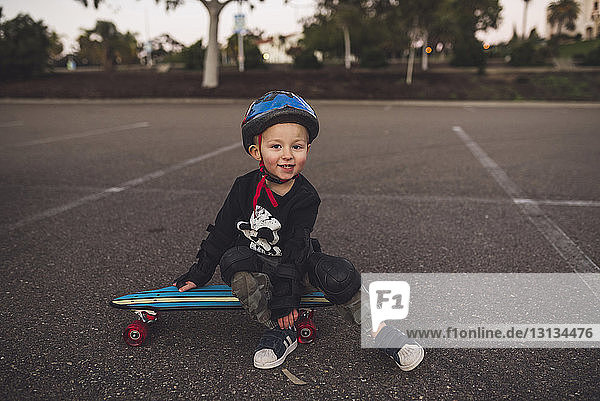 Porträt eines süßen Jungen  der auf einem Skateboard auf dem Feld sitzt
