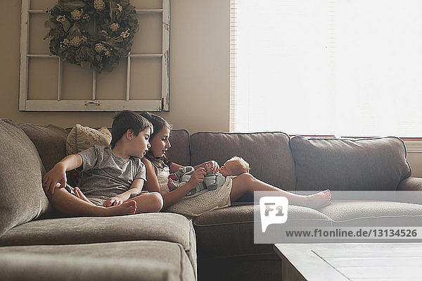 Geschwister spielen auf dem kleinen Jungen  während sie zu Hause auf dem Sofa sitzen