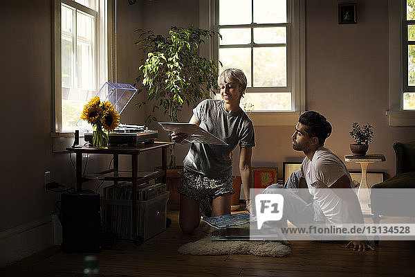 Man looking at woman holding vinyl record on floor at home