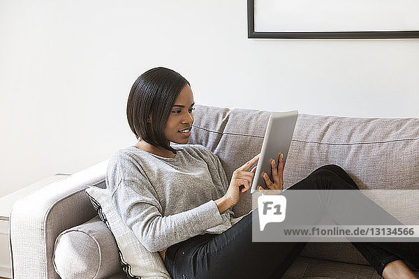 Frau benutzt Tablet-Computer auf dem Sofa zu Hause