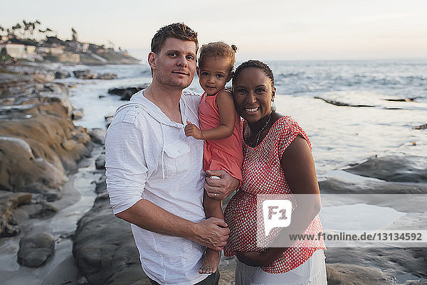 Portrait of happy parents with daughter at beach during sunset